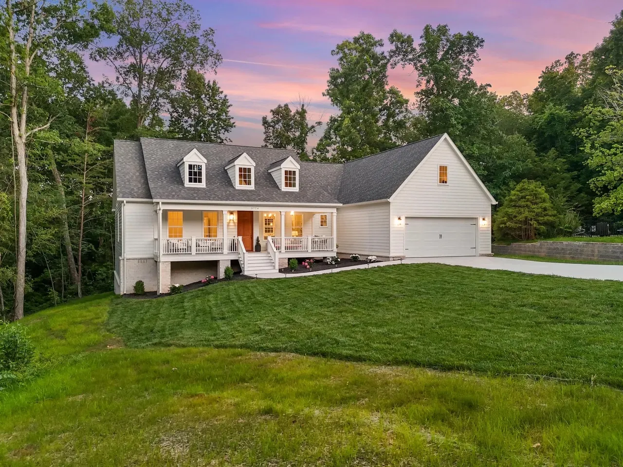 A white custom home by Ryabchuk Construction with dormers, a covered front porch and a two-car garage at dusk