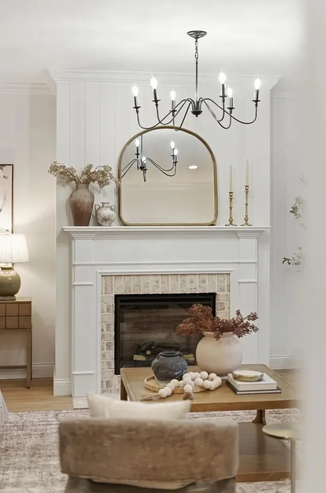 Living room with a whitewashed brick fireplace, white mantel and black iron chandelier