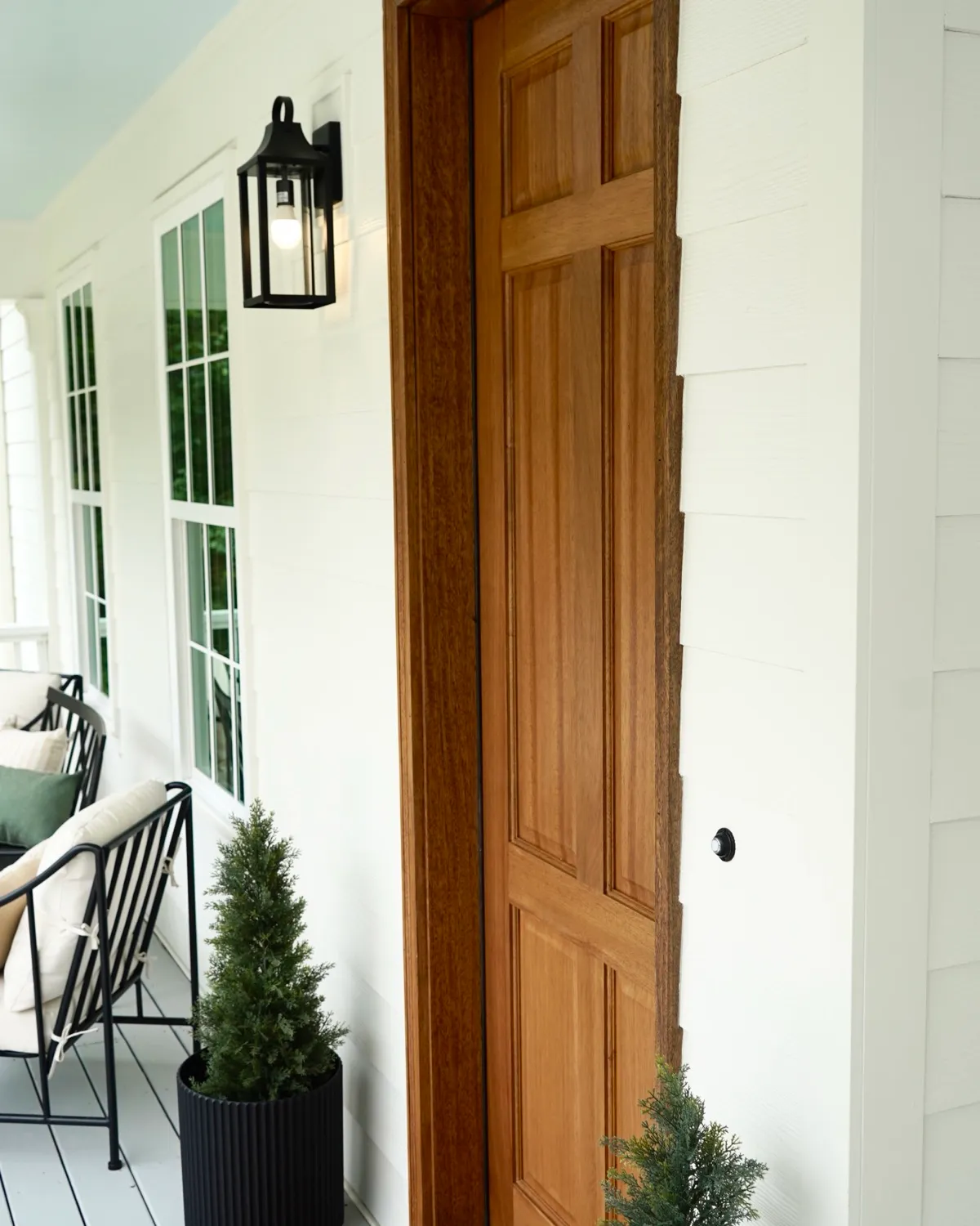 Covered front porch with a stained wood door, white siding and a black lantern