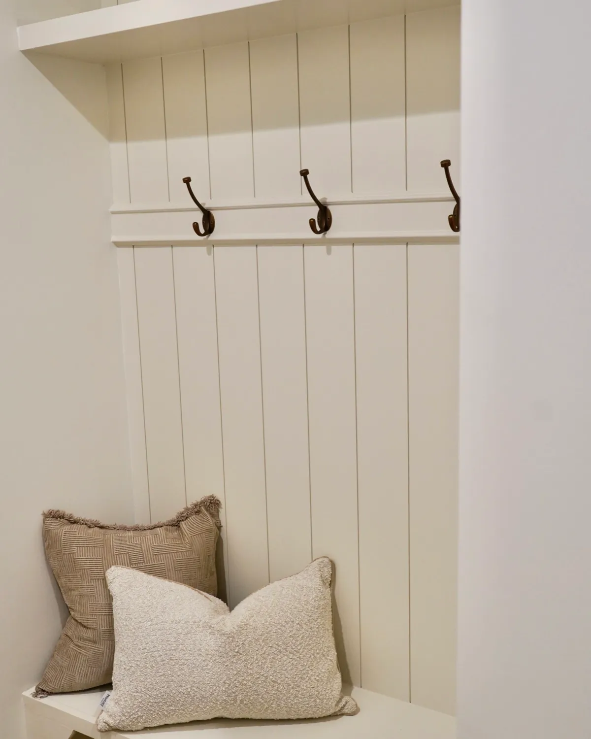 Built-in mudroom bench with vertical shiplap and black coat hooks