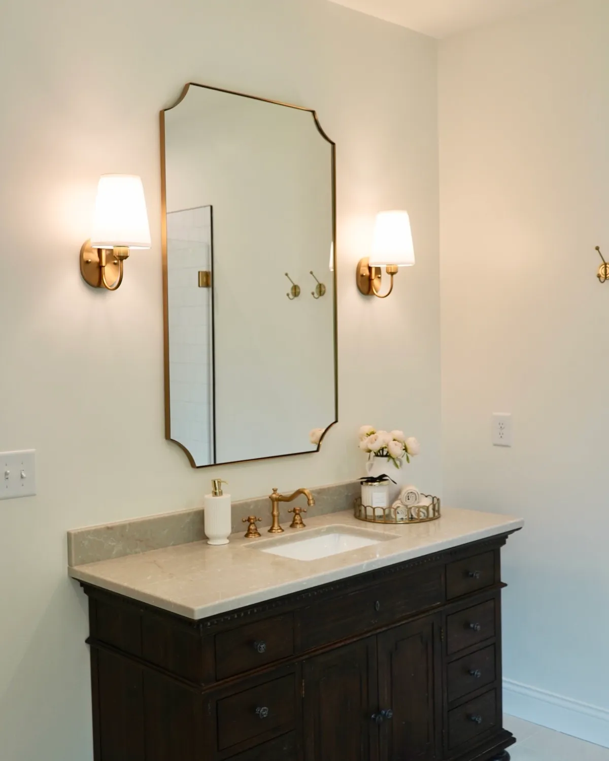 Bathroom vanity with a dark wood cabinet, stone top and brass fixtures under an arched mirror