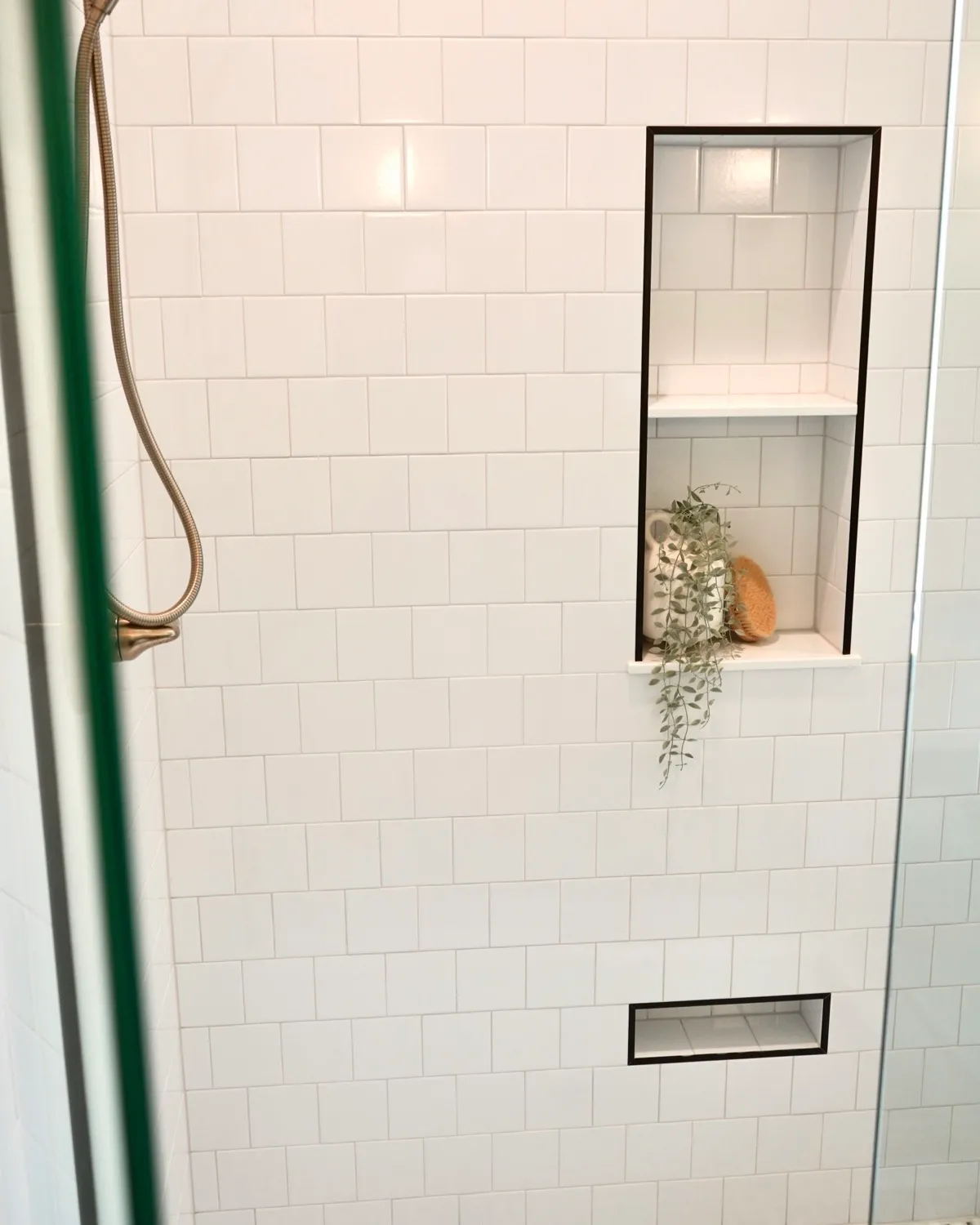 Walk-in shower with white tile, a black-trimmed niche and a brass handheld shower